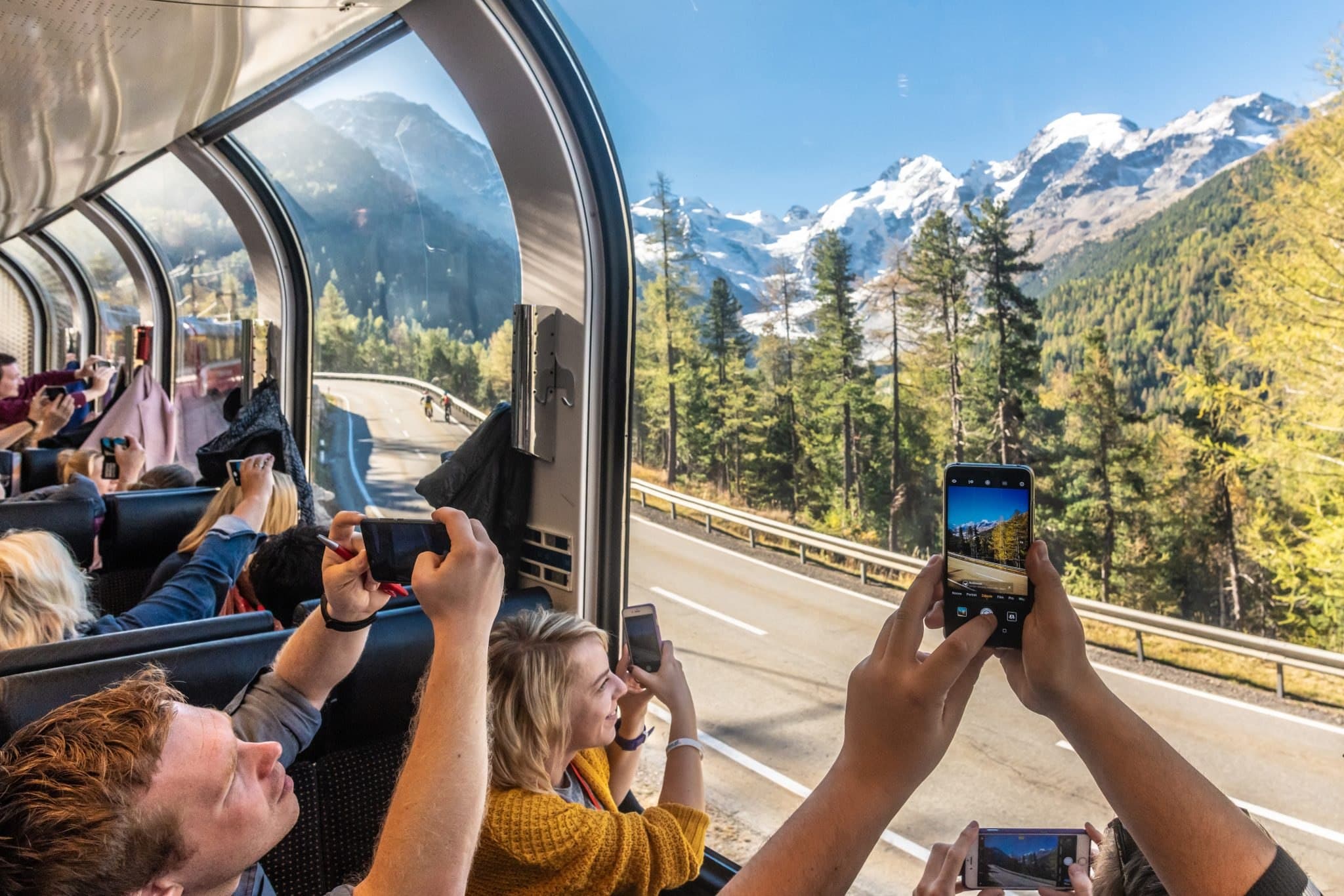 Travellers photographing snowy peaks from a panoramic train