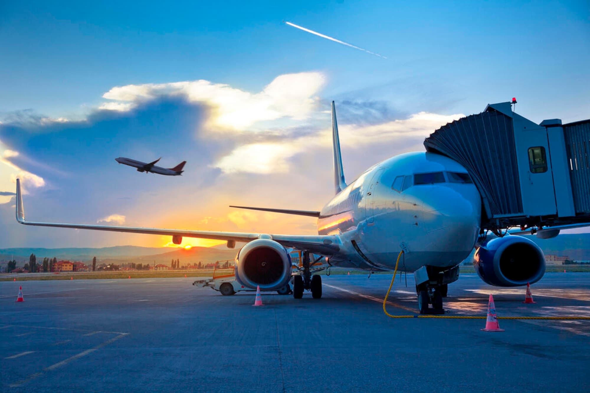 An airliner at the gate at sunset, another taking off behind it