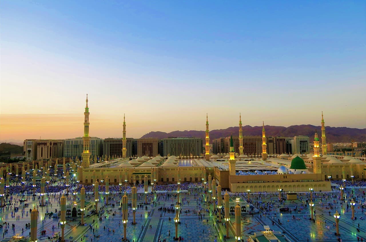 An expansive view of the Prophet's Mosque (Al-Masjid an-Nabawi) in Medina, Saudi Arabia, at dusk with its many minarets against a clear sky.